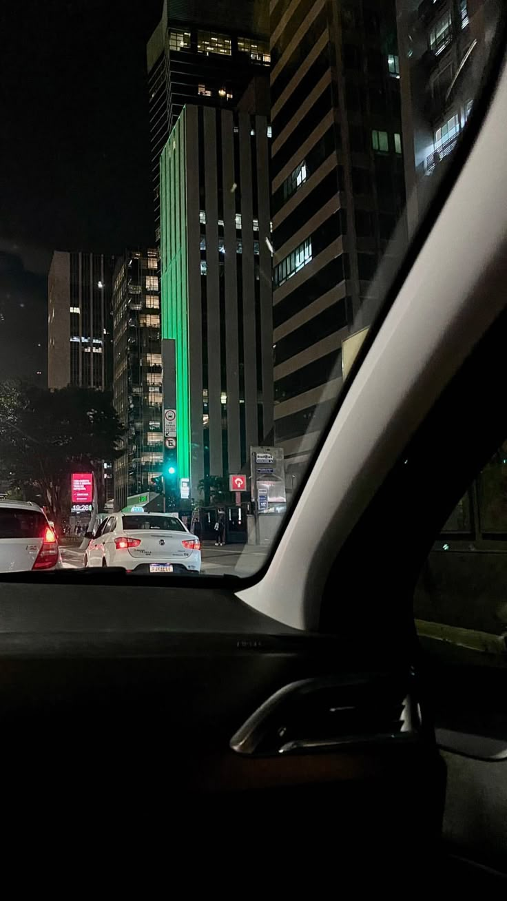 cars are driving down the street at night in front of tall buildings and skyscrapers