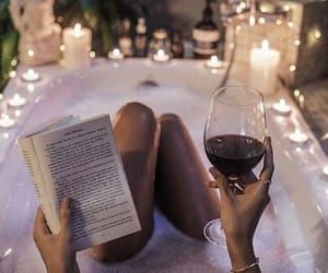 a woman is reading a book and holding a glass of wine in front of candles