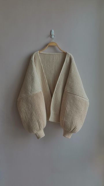 a white sweater hanging on a wall next to a wooden hanger with an object in it