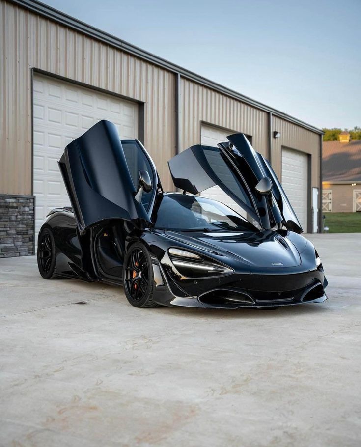 the black sports car is parked in front of a garage with its doors open and it's door opened