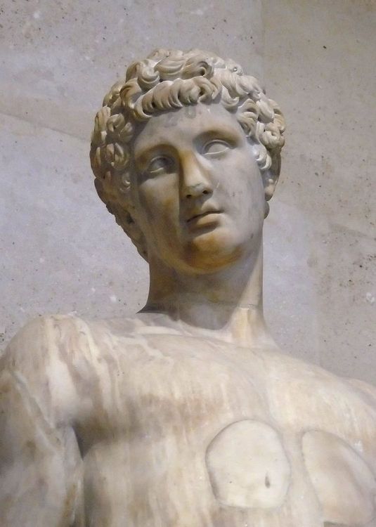 a marble statue of a man with curly hair and no shirt is shown in front of a wall