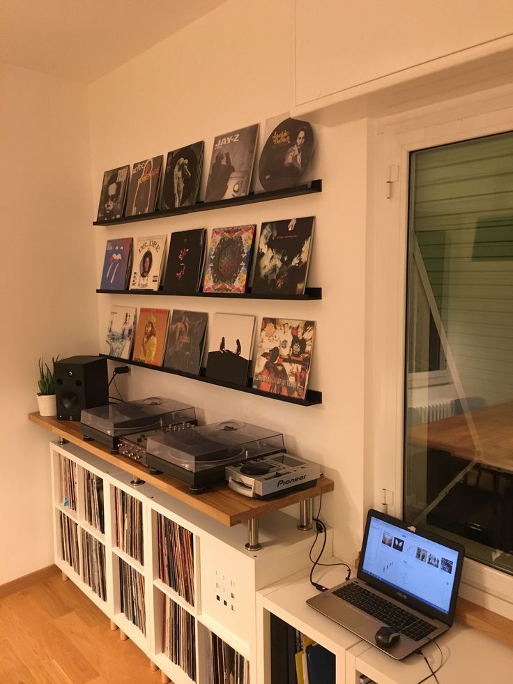 a laptop computer sitting on top of a wooden table next to a book shelf filled with records