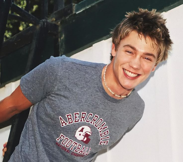 a young man is smiling and leaning against a wall with his hand on his hip