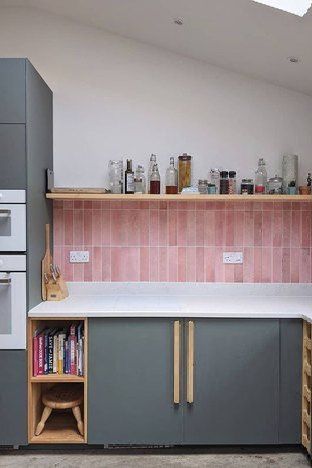 a kitchen with grey cabinets and pink tile backsplash, white counter tops and wooden shelves