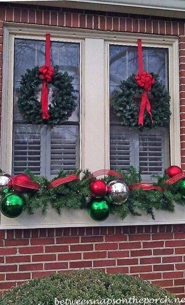 two christmas wreaths on the window sill with red and green ornaments hanging from them