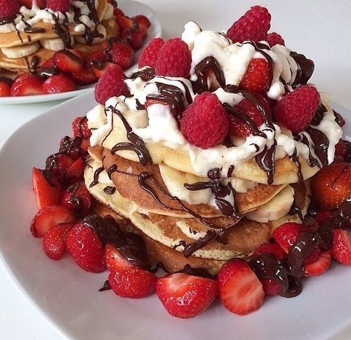 pancakes with whipped cream, strawberries and chocolate sauce on top are served on white plates