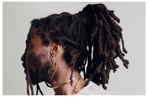 a man with dreadlocks wearing a white t - shirt and gold hoop earrings