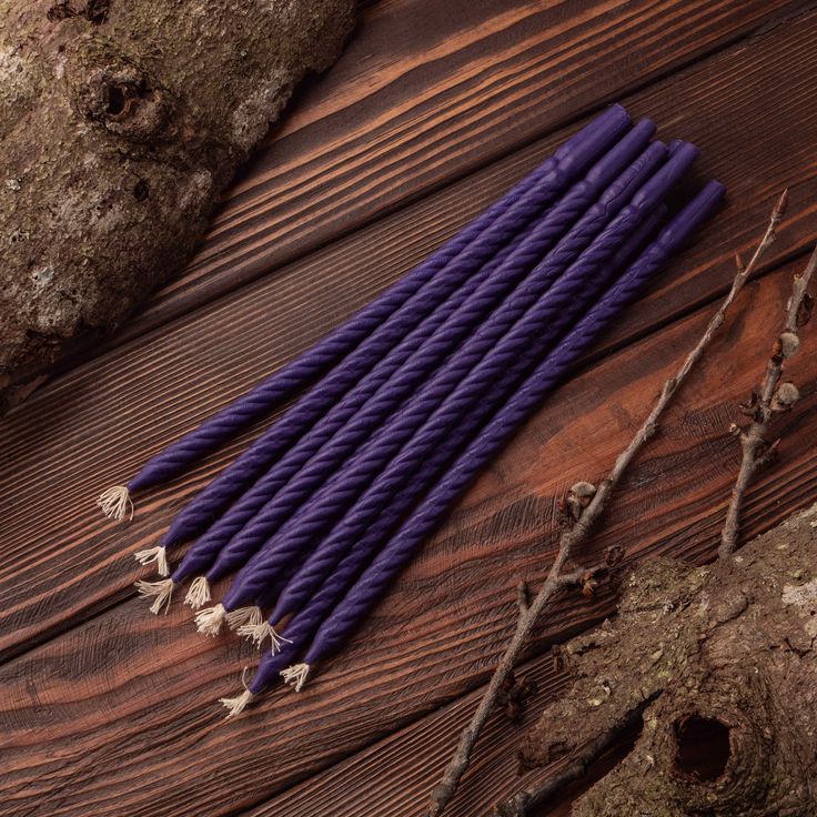 several purple candles sitting on top of a wooden table next to some branches and twigs