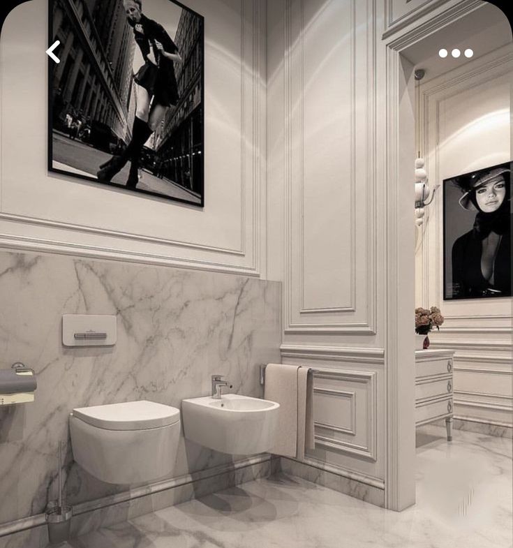 two white toilets in a bathroom with marble floors and walls, framed artwork on the wall