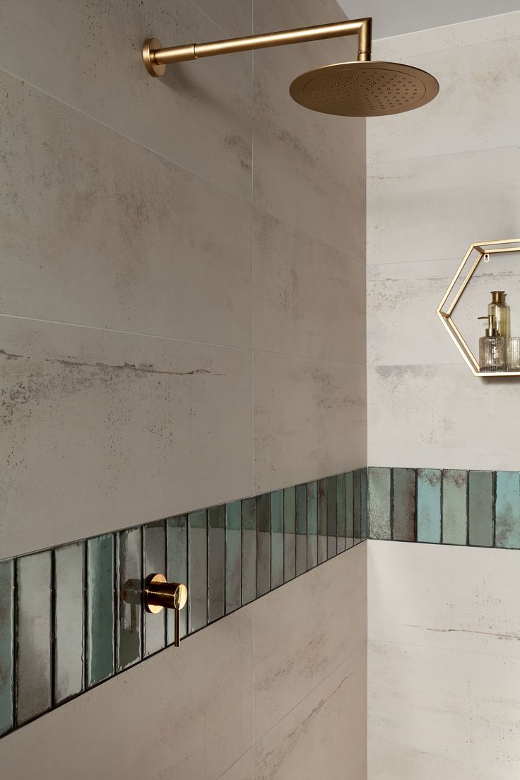 the shower head is mounted on the wall next to the tiled bathtub with gold faucet