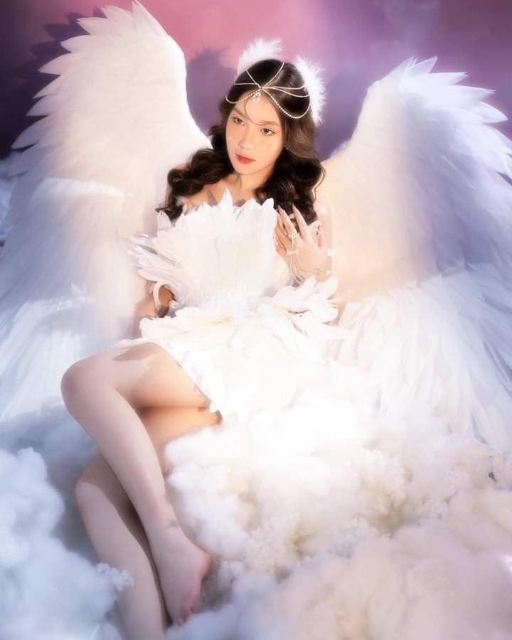 an angel sitting in the clouds with her hands on her chest and looking at the camera