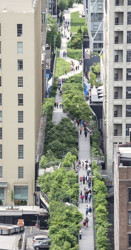 an aerial view of people walking down a street in a city with tall buildings and trees on both sides