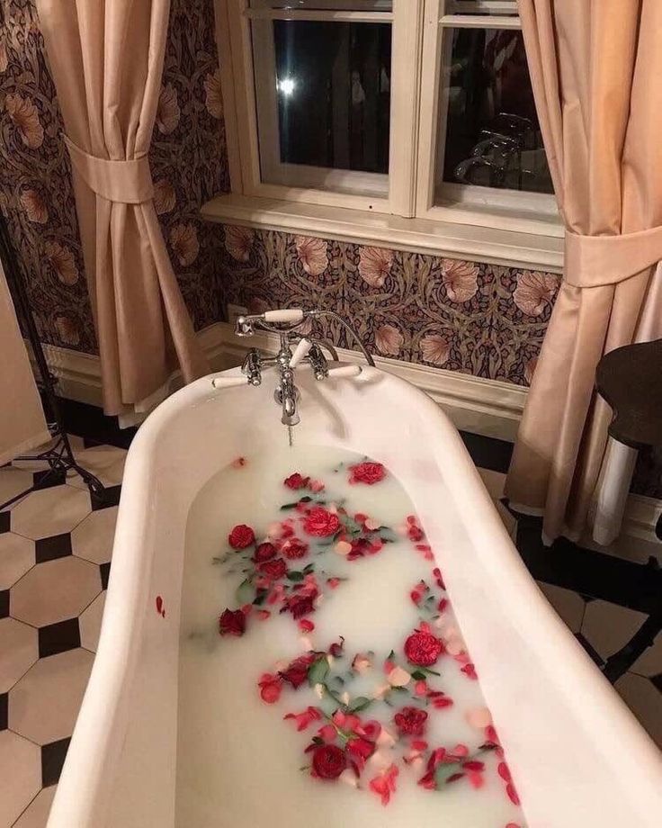 a bathtub filled with water and red roses on the floor next to a window