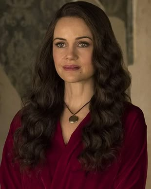 a woman with long dark hair wearing a red shirt and necklace looking at the camera