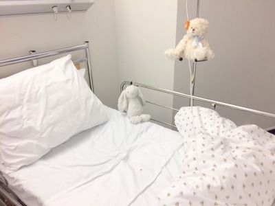 a white teddy bear sitting on top of a hospital bed next to a pillow and blanket