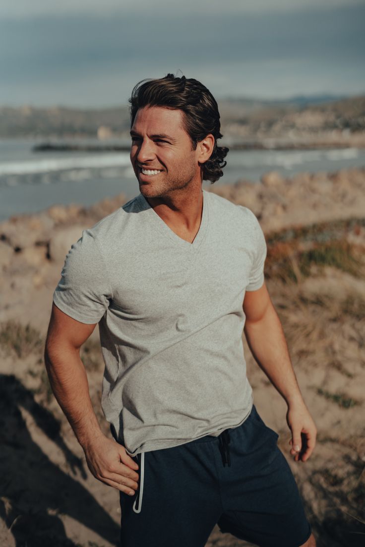 a man standing on top of a sandy beach next to the ocean with his hands in his pockets