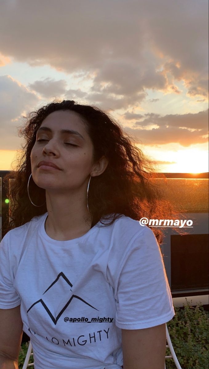 a woman sitting on top of a white chair next to a building with the sun setting behind her