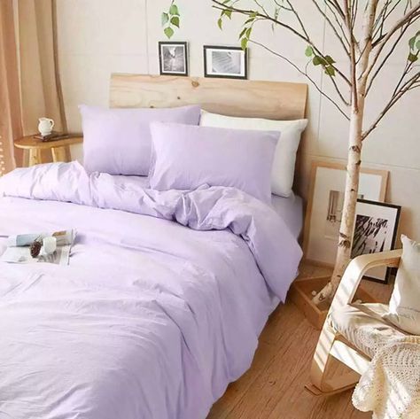 a bed with purple sheets and pillows in a room next to a small tree on the floor