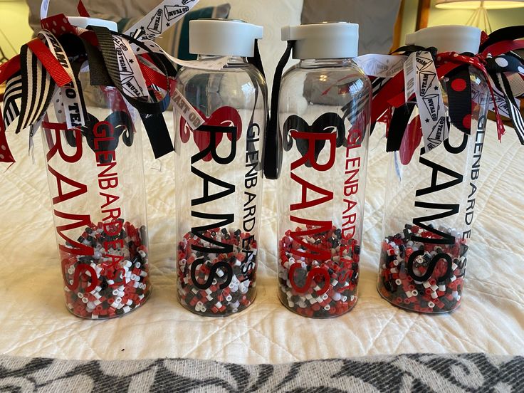 three water bottles with red, white and black confetti in them on a bed