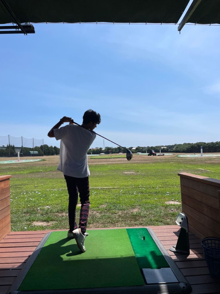 a person swinging a golf club at a green course on a sunny day in the sun