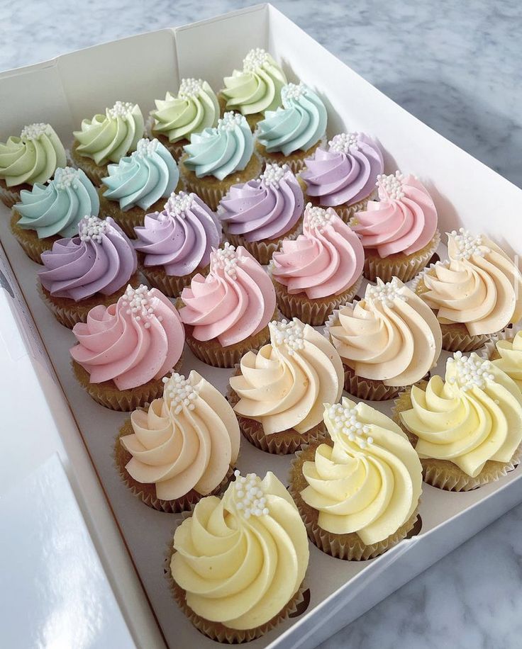 a box filled with lots of colorful cupcakes on top of a marble counter