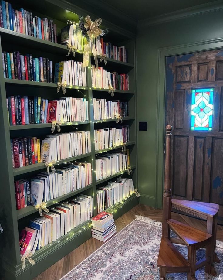 a room filled with lots of books next to a wooden chair and window covered in lights