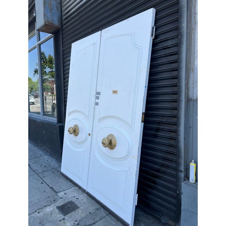 two white doors are leaning against the side of a building in front of a closed door