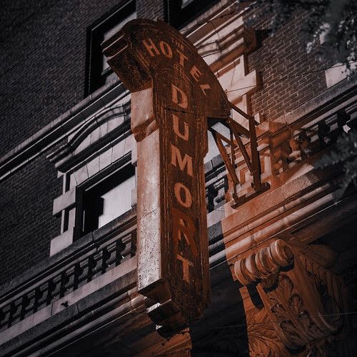 an old neon sign on the side of a building in front of a tall brick building