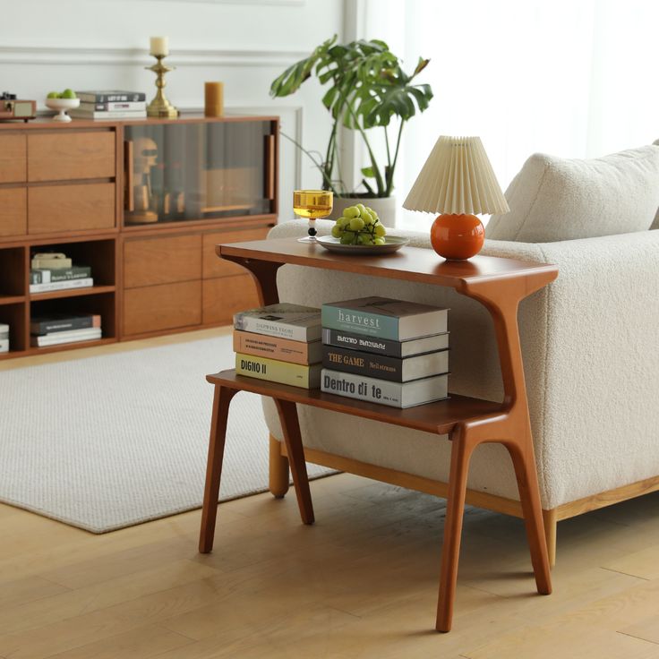 a white couch sitting next to a wooden table with books on it and a lamp