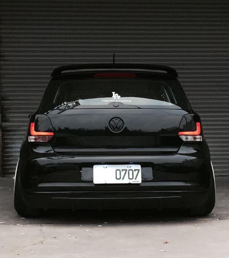 the back end of a black volkswagen car parked in front of a garage door with its trunk open