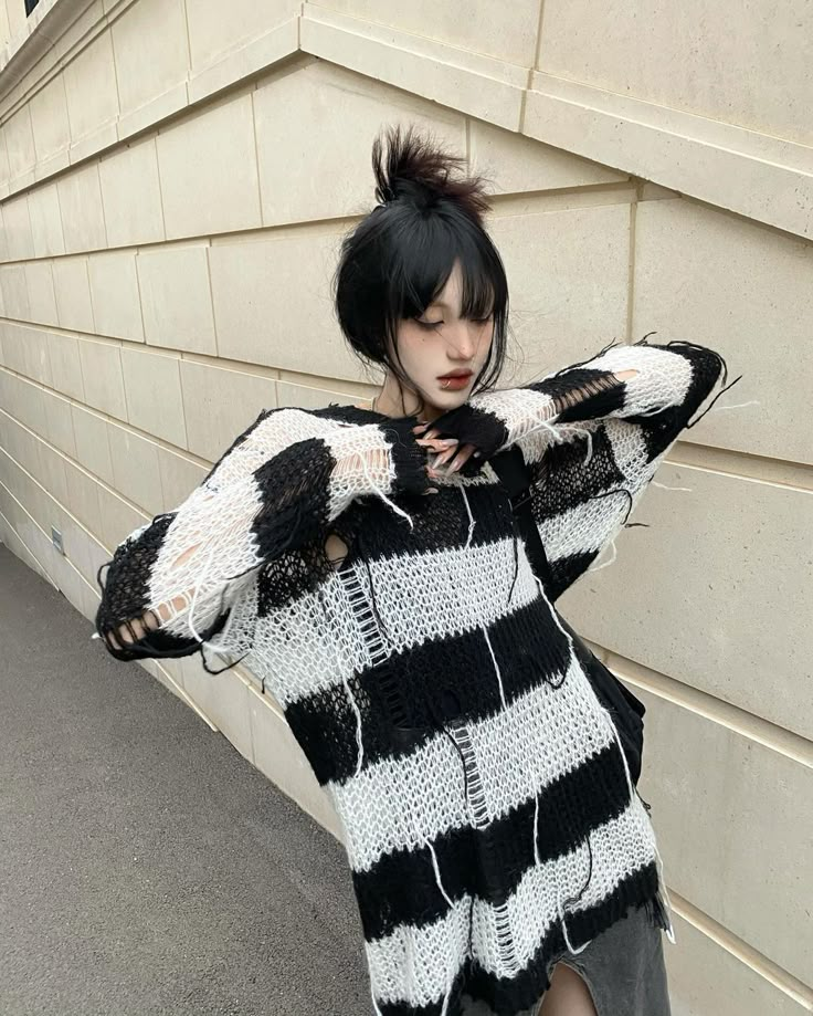 a woman with black and white hair is standing in front of a wall wearing an oversize sweater