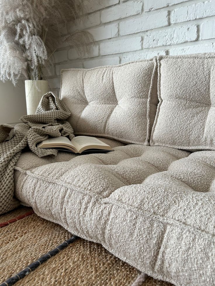 a couch that is sitting in front of a brick wall with a book on it