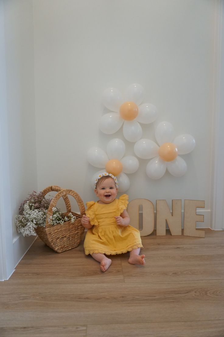 a baby sitting on the floor in front of balloons and a sign that says one