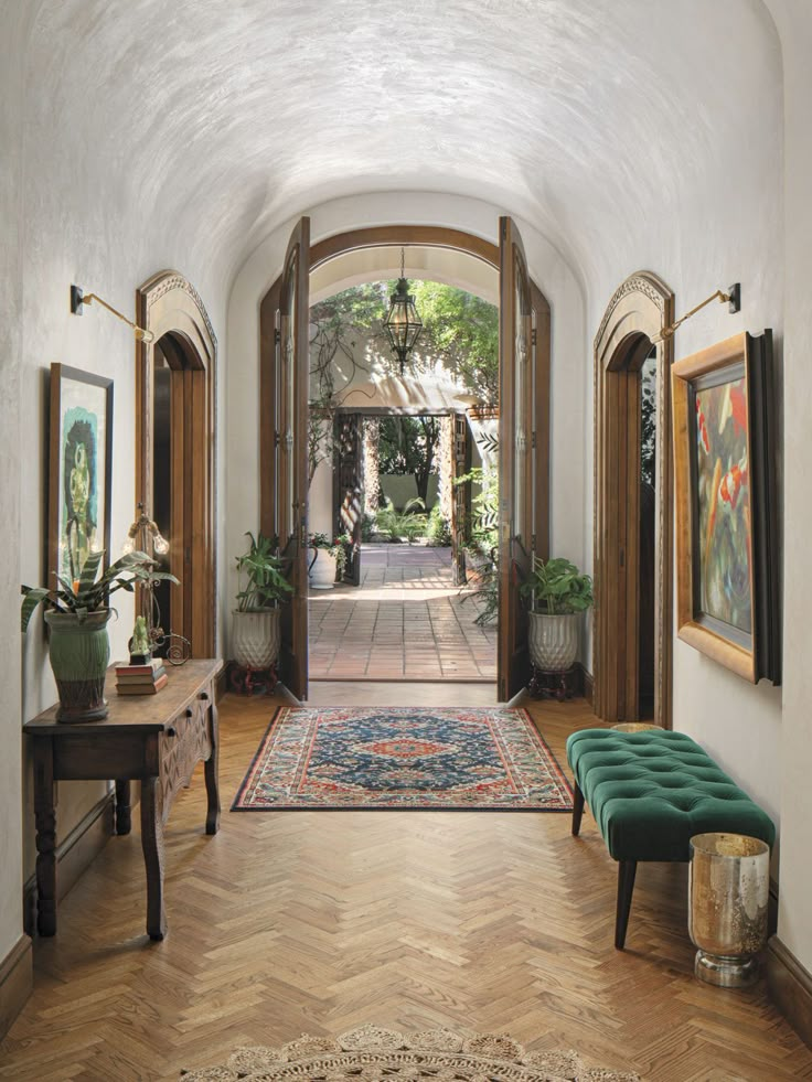 an entry way with wooden floors and green bench in the center, surrounded by potted plants