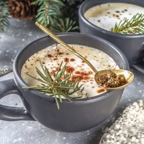 two mugs filled with hot chocolate and topped with sprig of rosemary next to pine cones