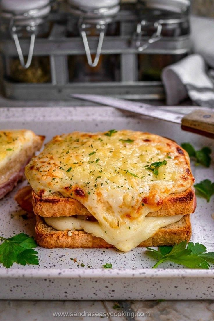 there is a sandwich with cheese and parsley on the plate next to some utensils