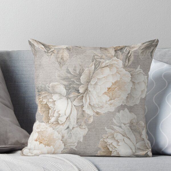 a white and beige floral pillow sitting on top of a gray couch next to pillows