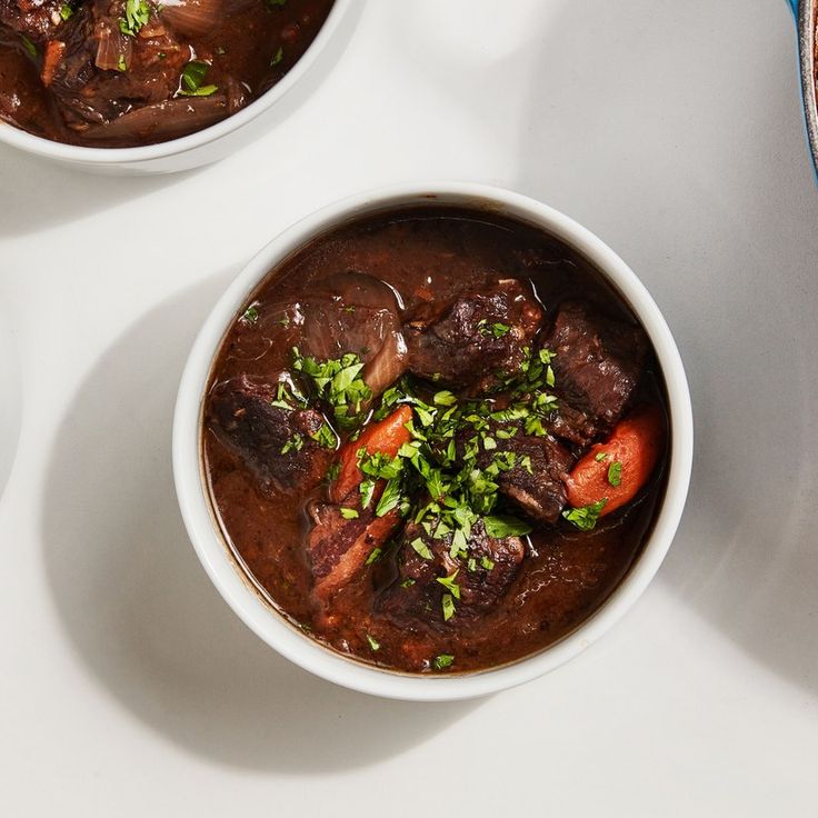 two bowls filled with beef stew on top of a white table