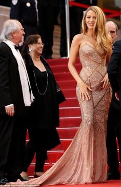 a woman in a long dress standing on the red carpet next to some men and women