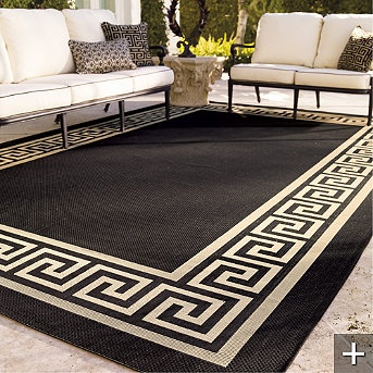 a black and white area rug with greek border on the ground next to couches