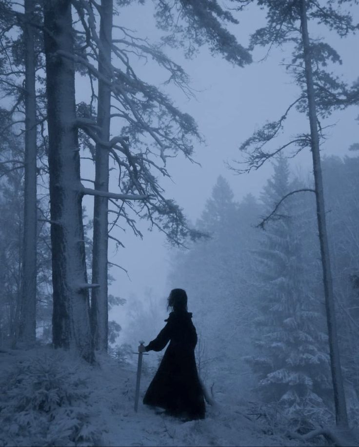 a woman walking through the woods on a snow covered trail with an ax in her hand