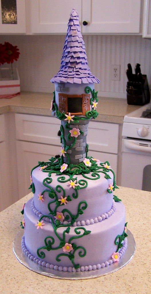 a three tiered cake decorated with flowers and a purple house on top is sitting on a kitchen counter