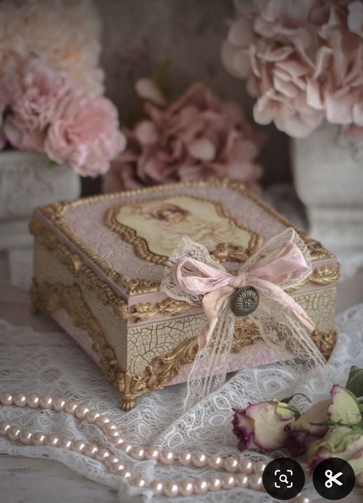 there is a small box with a bow on it and pearls around the edges next to flowers