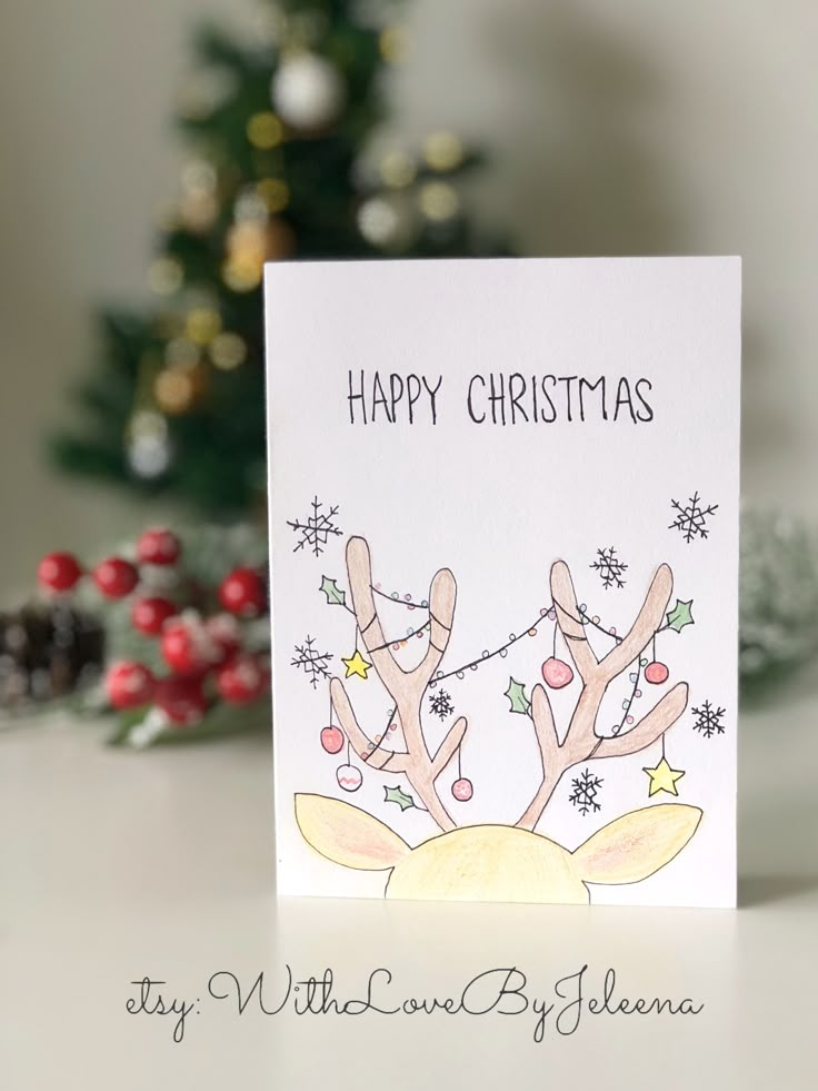 a handmade christmas card with reindeers on the front and side, in front of a christmas tree