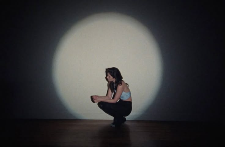 a woman squatting in front of a white circle with her hands on her knees