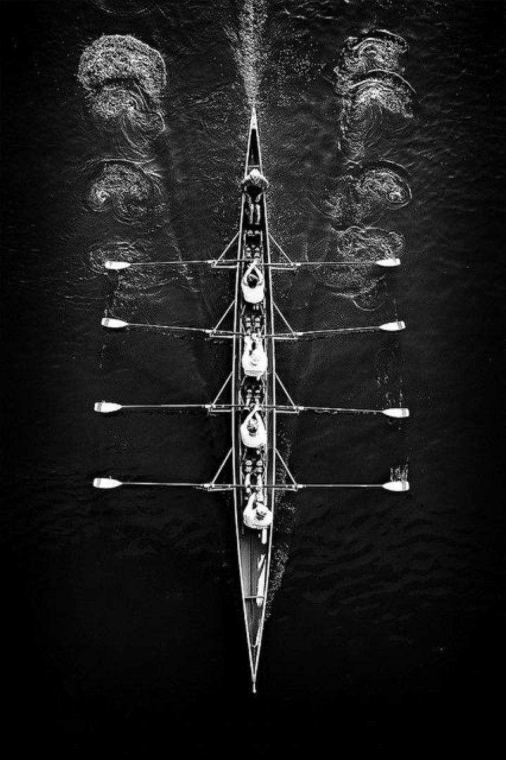 an aerial view of a rowing boat with eight rowers in the water, taken from above