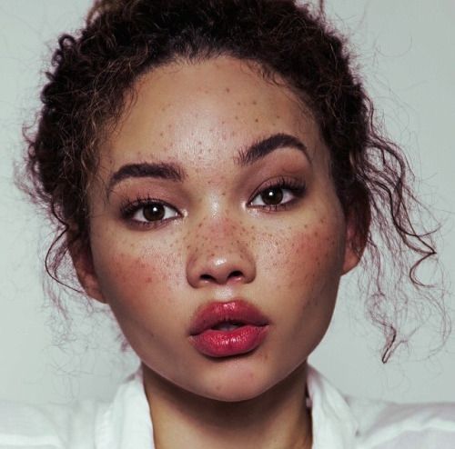 a woman with freckles on her face is posing for the camera while wearing a white shirt