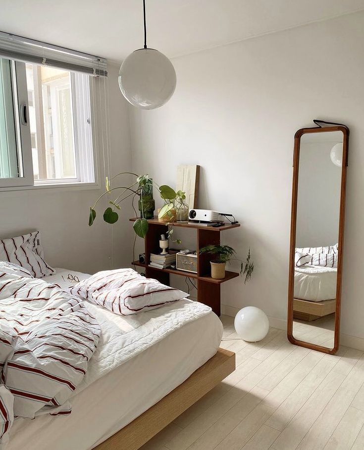 a bedroom with a bed, mirror and plant on the floor in front of it