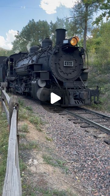 an old fashioned train is on the tracks next to a wooden rail road track and some trees