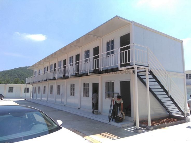 two people are standing in front of a white building with black balconies on the second floor